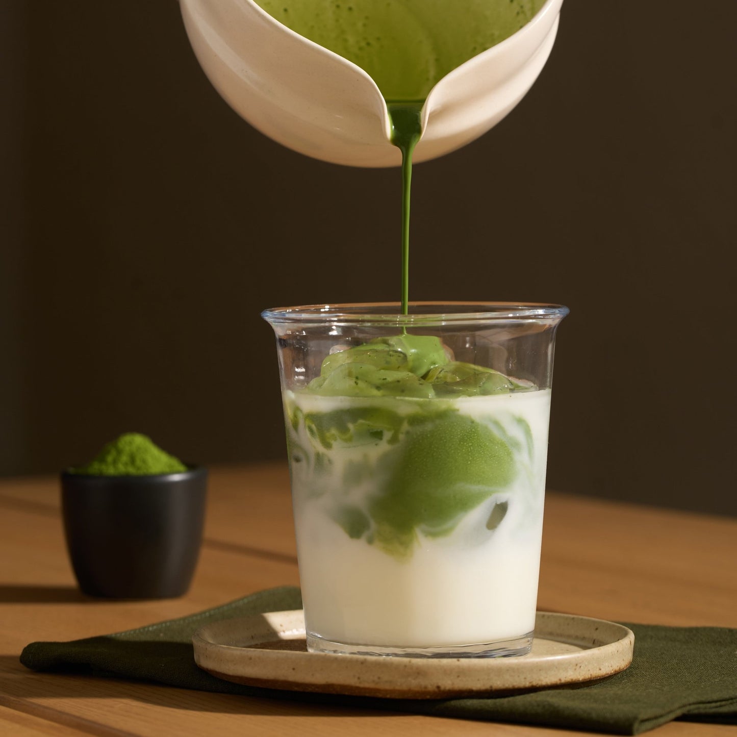 Presentation d’un Matcha latte avec une coupelle remplie de matcha en poudre en arrière plan